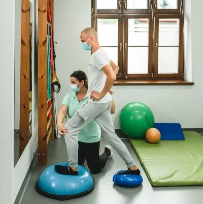 Fizjoterapeutka prowadzi ćwiczenia równowagi z pacjentem na sali kinezyterapii
