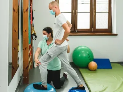 Fizjoterapeutka prowadzi ćwiczenia równowagi z pacjentem na sali kinezyterapii